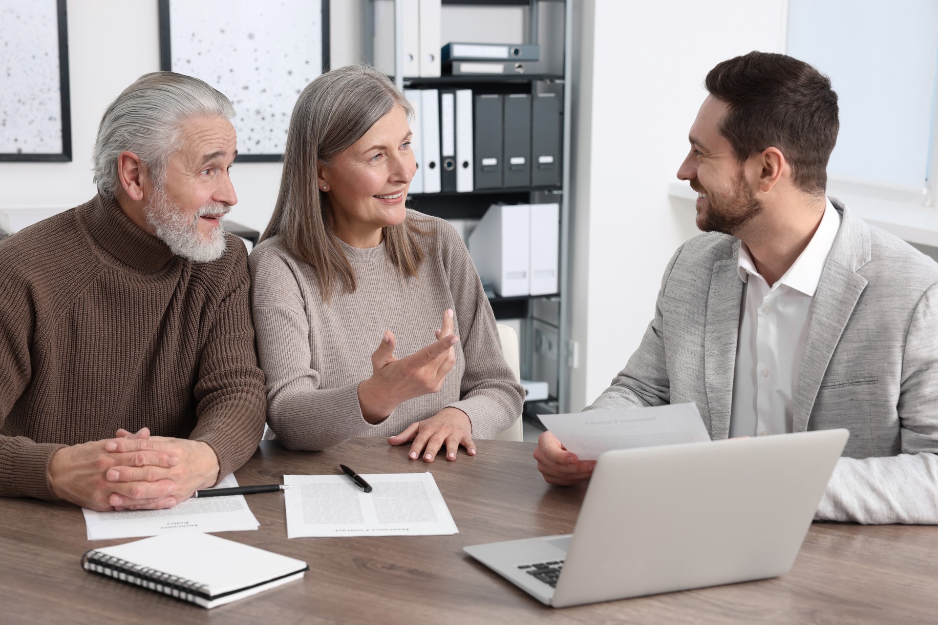 Elderly couple consulting insurance agent about pension plan at wooden table indoors