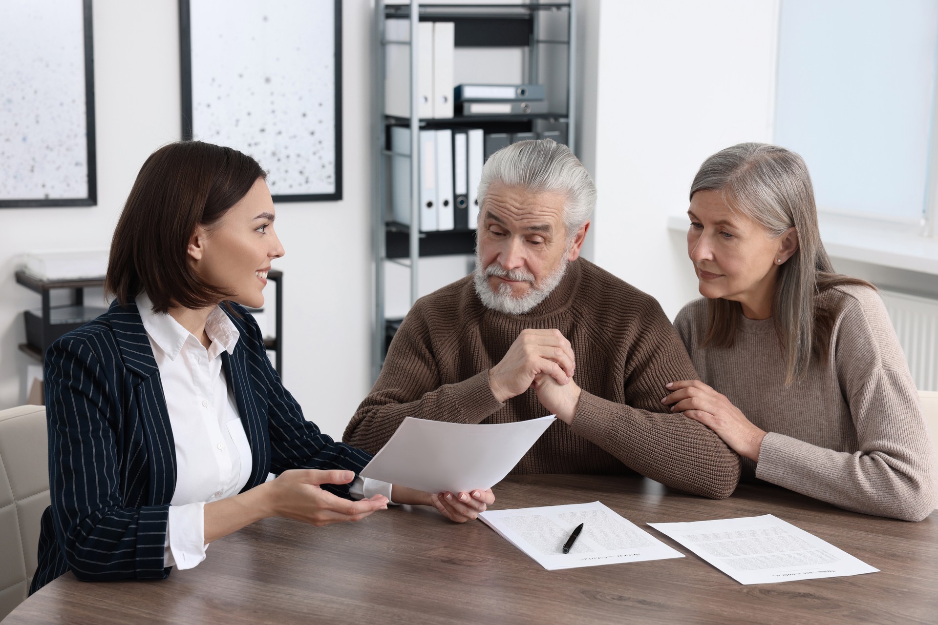 Elderly couple consulting insurance agent about pension plan at wooden table indoors